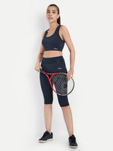 ALT text: Model holding a tennis racket wearing Waylene's navy blue capri tights and matching sports bra, highlighting the outfit's suitability for sports activities.